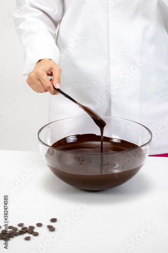 Closeup female chef stirring and pouring dark melted chocolate isolated on white background. Chocolatier make organic couverture high-quality hand-crafted chocolate. Candymaking, confectionery concept