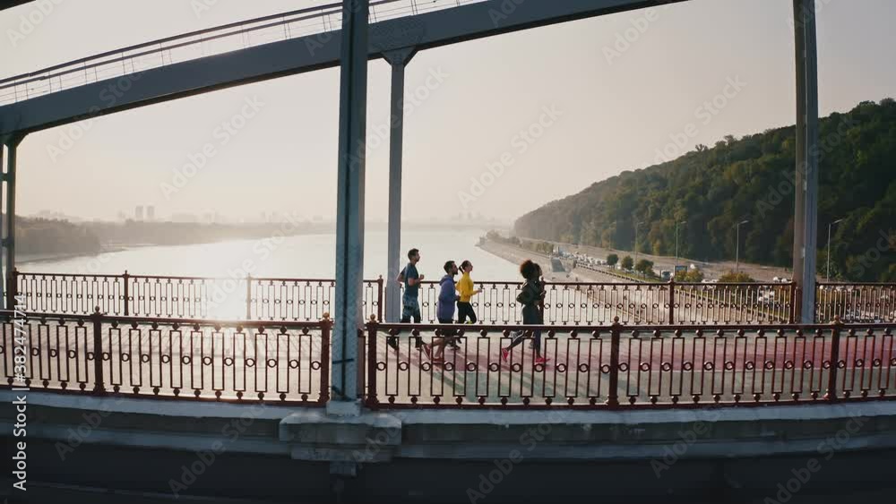 Morning workout concept, side view from drone at group of five runners training on bridge early in morning