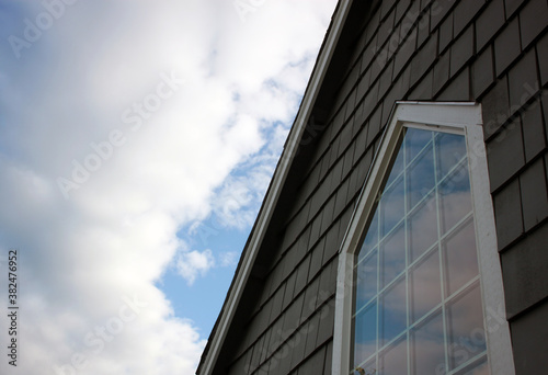 Large window with cloud reflections surrounded by white trim and gray shingles