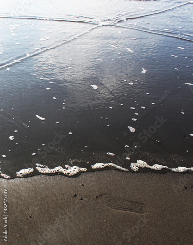 Shot of incoming tide line with stripe of sandy beach with a single foot print