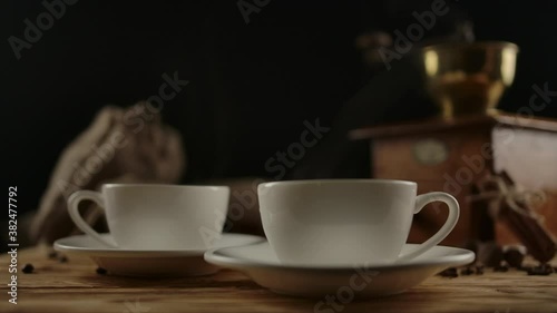 Female hand serves second modern coffee cup. Rotating wood table with first porcelain cup, traditional coffee mill, coffee beans bag, spices. Coffee break for couple. Duplicating the drink. Dolly shot