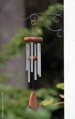 Decorative metal and wooden wind chimes hung outside from a curling hook
