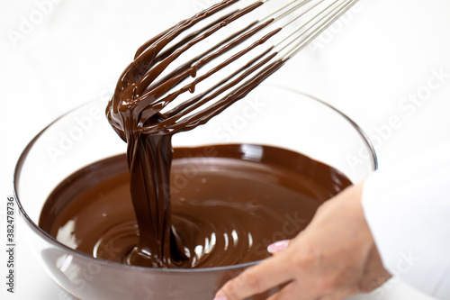 Mixing smooth delicious melted dark chocolate with whisk in glass bowl. Closeup. Organic chocolate icing to prepare confectionery. Making pralines chocolate candy truffle, pastry bakery patisserie