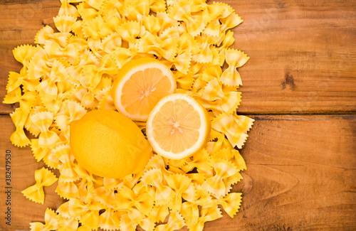 Dry pasta butterflies and lemons on a wooden background. Colorful pasta, typical southern Italian cuisine. Top view. High quality photo. Free space for text