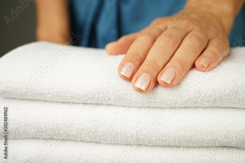 woman in a turquoise silk robe with beautiful hands with a good manicure holds a neatly folded pile of white terry towels indoors