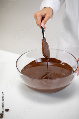 Close up stirring and pouring dark melted chocolate isolated on white background. Chocolatier make premium hand-crafted couverture chocolate. Candymaking, pastry production, bakery, dessert concept