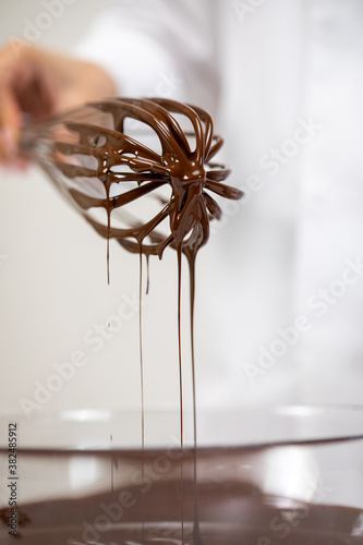 Close up sweet tasty dark melted chocolate on whisk isolated on white background. Chocolatier making premium hand-crafted chocolate. Preparing pralines, chocolate candy or truffles concept