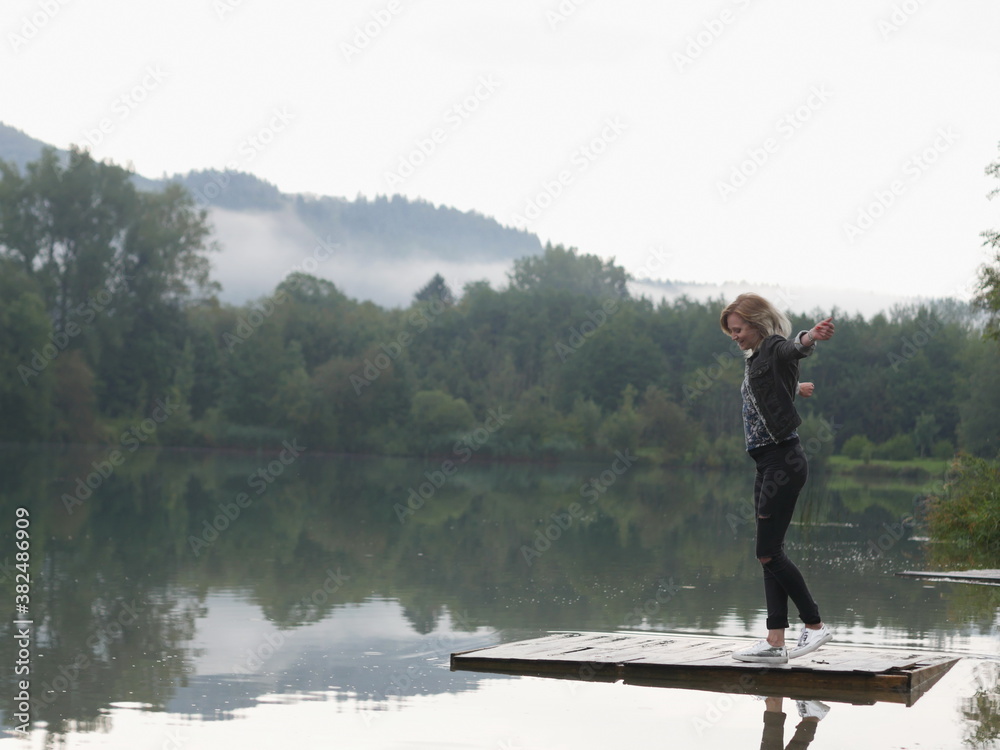 Happy blonde woman with arms widened on platform on water Happy blonde woman with arms widened on platform on water