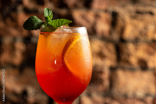 Aperol spritz cocktail in big wine glass with bloody oranges decorated with peppermint, summer Italian fresh alcohol cold drink. Bricks bar wall background, selective focus photo