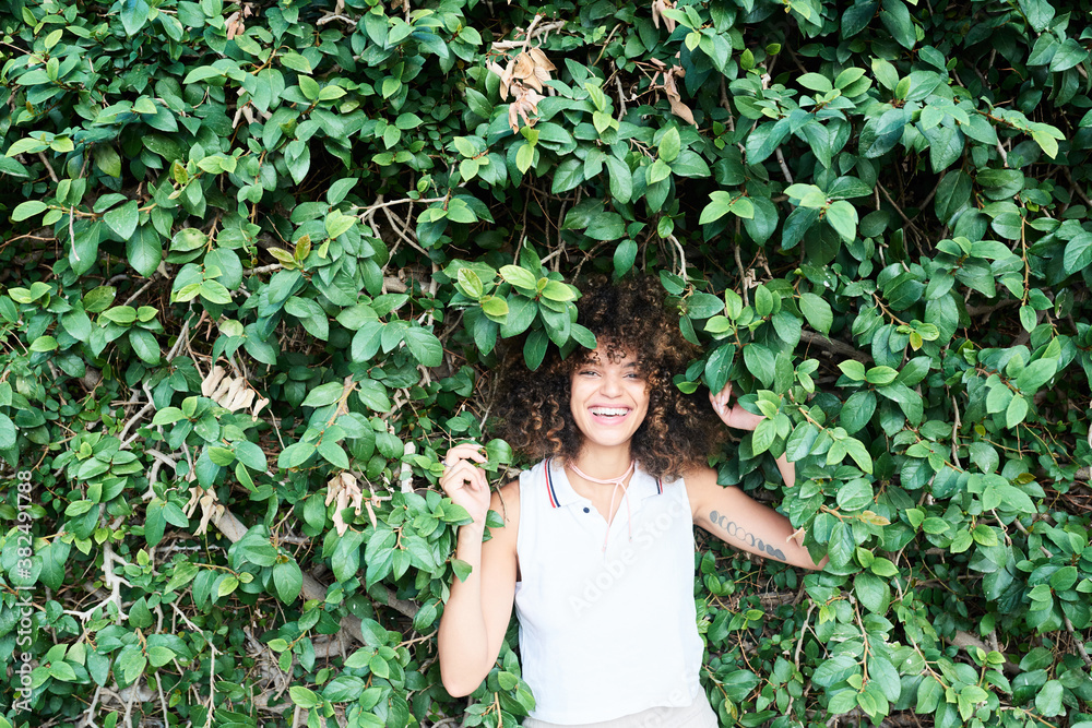 Smiling brunette with afro and tattoo on arm in green hedge Smiling brunette with afro and tattoo on arm in green hedge