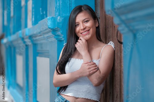 happy hispanic woman with long smiling black hair leaning on a wooden side view door