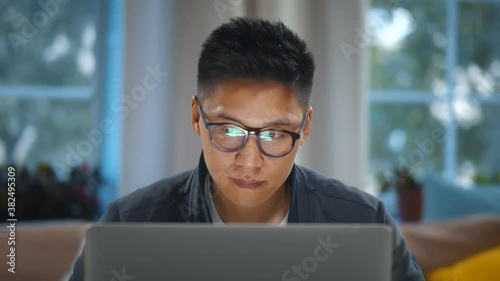 Close up of young asian man in glasses working on laptop at home office