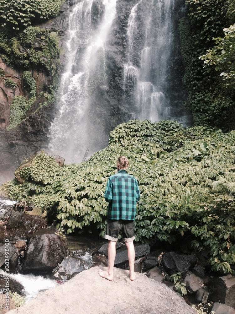 Young man standing in front of waterfall Young man standing in front of waterfall