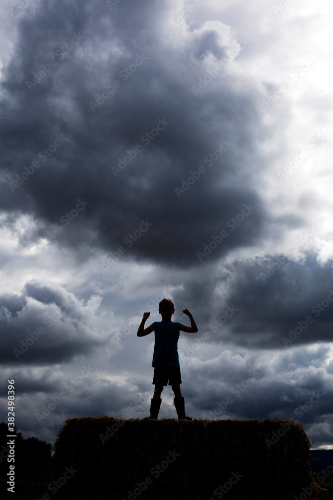 Silhouette of boy flexing his muscles against a dark cloudy sky Silhouette of boy flexing his muscles against a dark cloudy sky