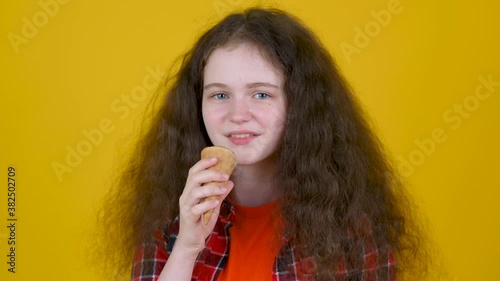 Close up portrait of young girl with curly hair in shirt eating ice cream isolated on yellow studio background