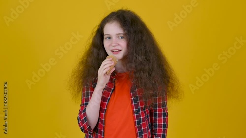 Happy girl with curly hair in shirt eating ice cream isolated on yellow studio background