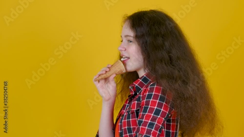 Funny girl with curly hair eating ice cream isolated on yellow studio background