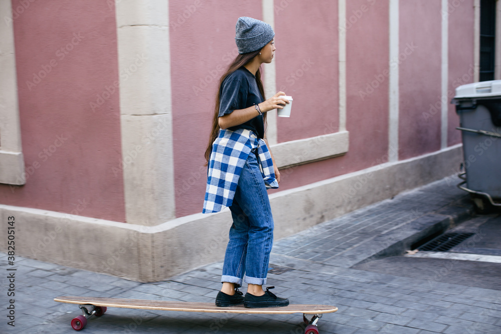Skater girl drinking a coffee riding a longboard on the street. Skater girl drinking a coffee riding a longboard on the street.