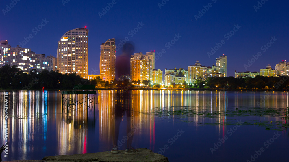 A guy stands on the banks of the Dnieper river against the background of a bright night embankment