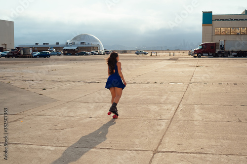 Woman in blue dress on roller skates riding around an airfield
