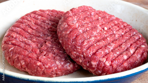 Two raw hamburger patties that are lightly seasoned with salt and pepper, sitting outside in order to reach room temperature before putting them on the grill. Raw meat and food preparation concept.