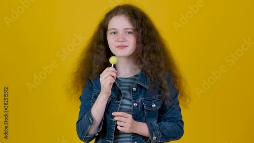 Portrait of young girl with curly hair with candy isolated on yellow background