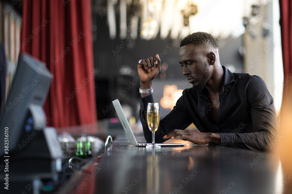handsome young African American man looking at laptop computer screen. Black businessman working on laptop computer at the club.