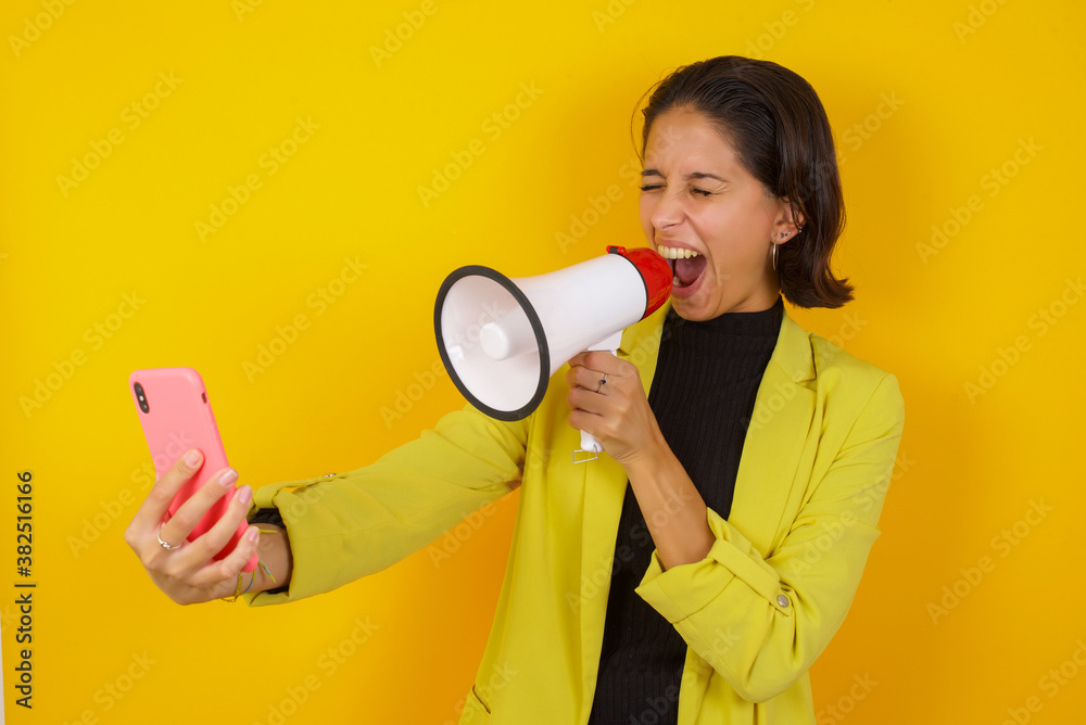 Crazy impressed Young hispanic businesswoman wearing casual turtleneck sweater and jacket use cell phone reads incredible news on social media information stare, screams with megaphone Crazy impressed Young hispanic businesswoman wearing casual turtleneck sweater and jacket use cell phone reads incredible news on social media information stare, screams with megaphone