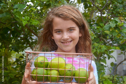 Smiling girl holding a basket of freshly picked limes in front of a lime tree
