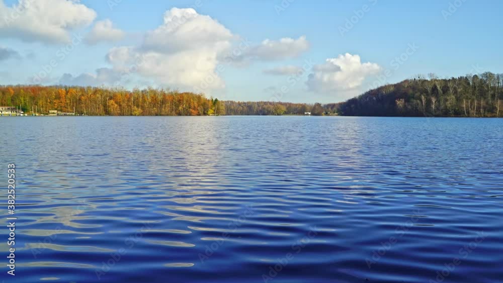 Afternoon sunlight on clear lake in autumn, forest in distance and white clouds