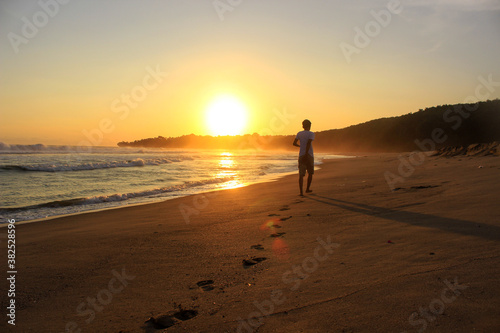 A man walks toward the setting sun, leaving footprints in the sand. Far look from behind.  © Artanto