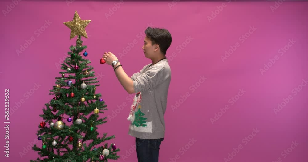Studio shot of an undecided man decorating a christmas tree, slow motion Studio shot of an undecided man decorating a christmas tree, slow motion