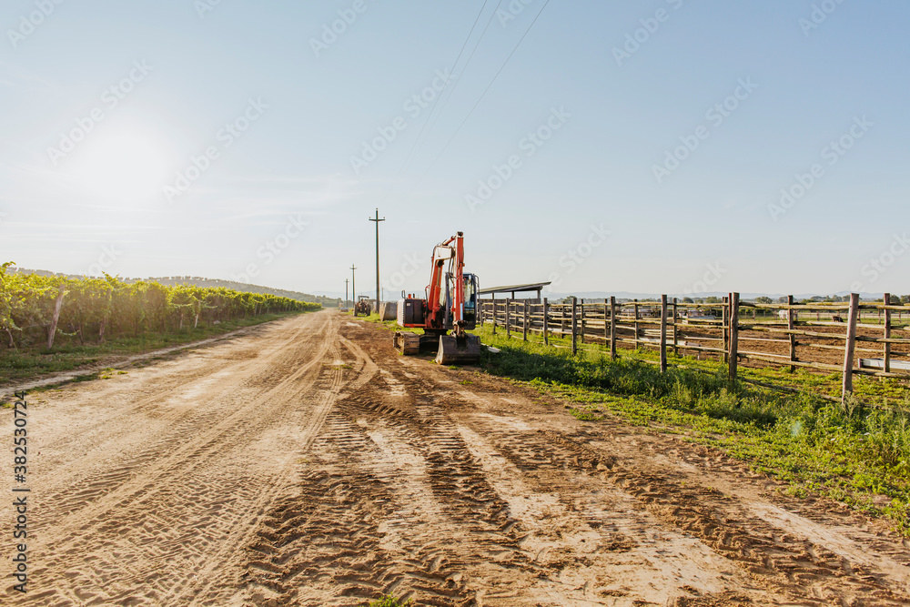 Bulldozers parked at farm's roadside close to vineyard and pasture corral at sunset Bulldozers parked at farm's roadside close to vineyard and pasture corral at sunset