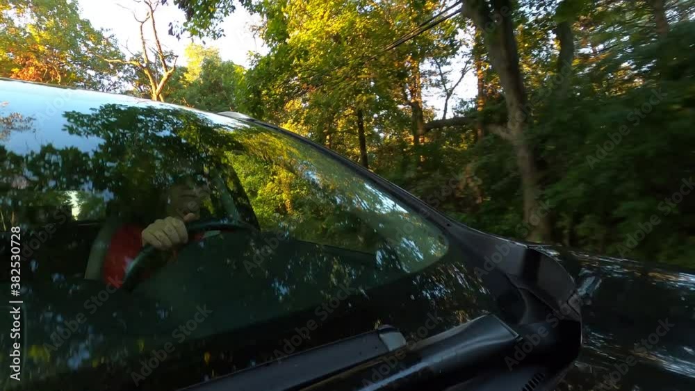 Woman driving a black car at sunrise, sunset. Sunlight flashes on the face. The camera is outside the car Woman driving a black car at sunrise, sunset. Sunlight flashes on the face. The camera is outside the car