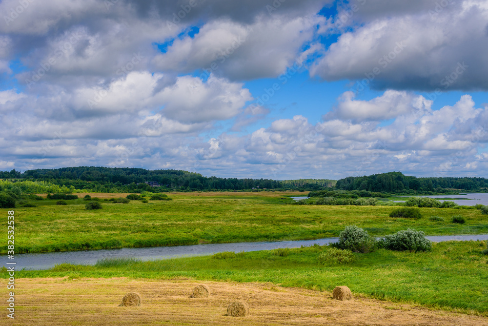 Stunning landscape with river, field, haystacks and gorgeous clouds in the sky