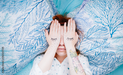 woman lying in bed coverig her eyes with her hands with eyebrows painted photo