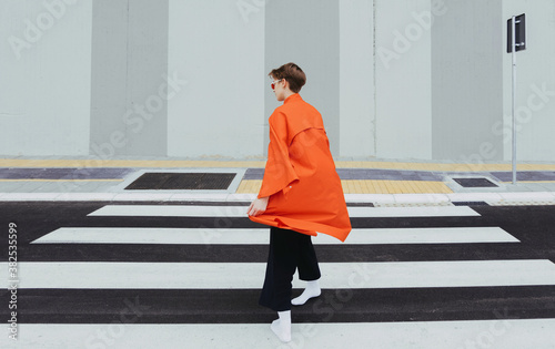 Alternative stylish young female on orange/red coat on street/minimalist composition.