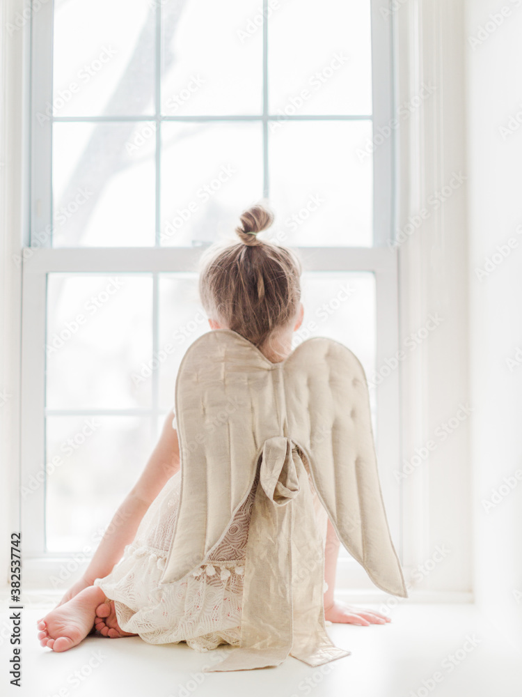 little girl playing dress up with angel wings sitting at a window little girl playing dress up with angel wings sitting at a window