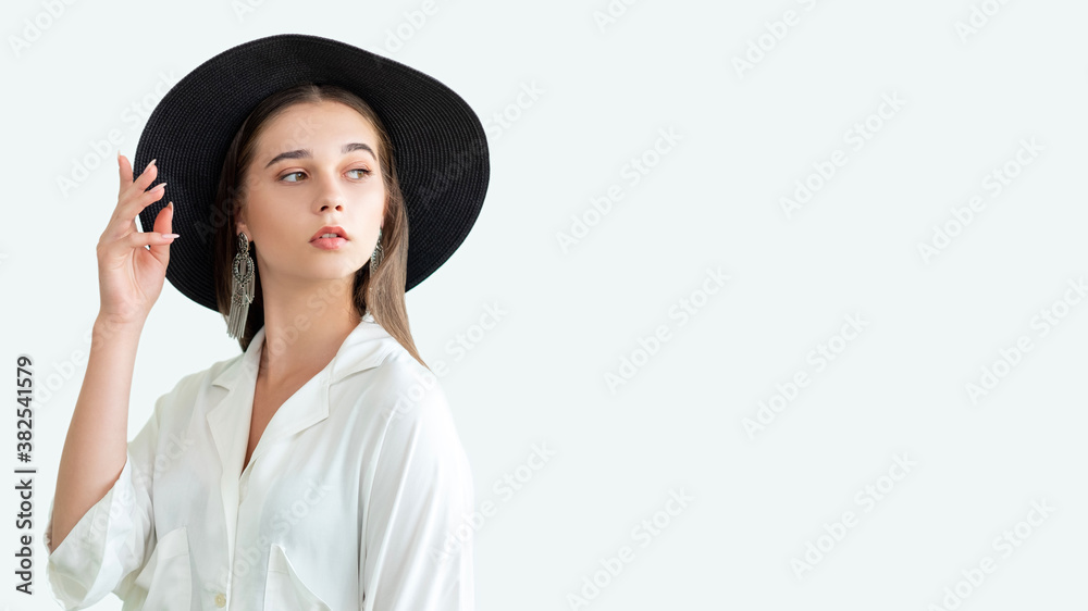 Trend summer look. Casual fashion outfit. Stylish woman in wide-brimmed black hat vintage earrings white shirt isolated on neutral copy space. Boho lifestyle. Advertising background Trend summer look. Casual fashion outfit. Stylish woman in wide-brimmed black hat vintage earrings white shirt isolated on neutral copy space. Boho lifestyle. Advertising background