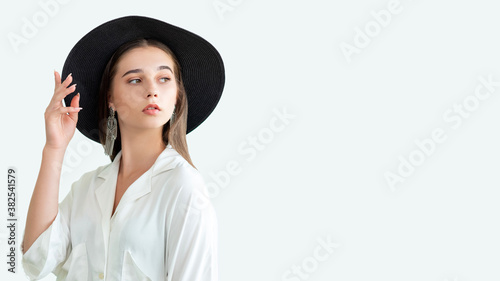 Trend summer look. Casual fashion outfit. Stylish woman in wide-brimmed black hat vintage earrings white shirt isolated on neutral copy space. Boho lifestyle. Advertising background