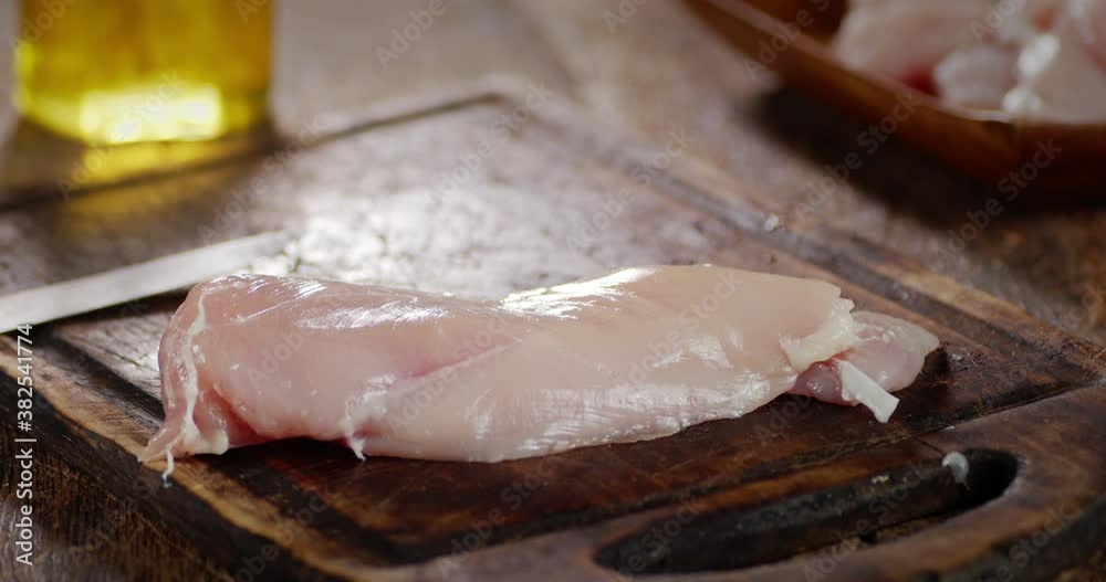 The men's hand puts raw chicken fillet on a cutting board. The men's hand puts raw chicken fillet on a cutting board.