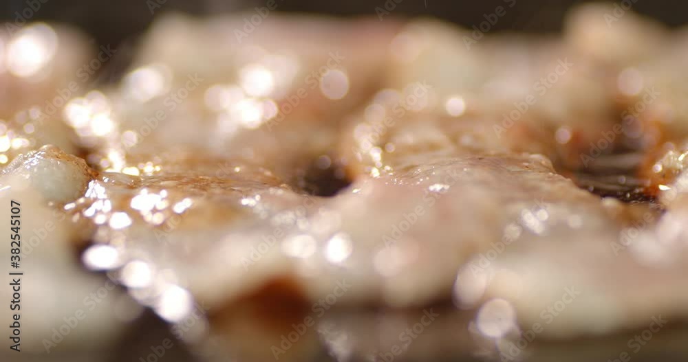 Bacon for the burger is fried with bubbles of oil in a pan.
