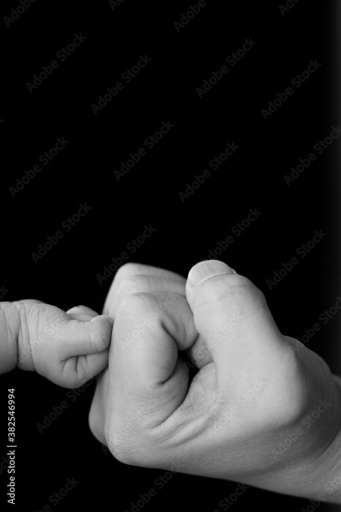 B&W photo,Fist of Dad and Newborn Baby,isolated on black background.