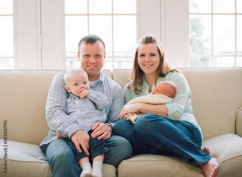 Young family sitting on a couch with their new baby Young family sitting on a couch with their new baby