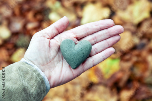 Hand holding a rock heart over a fall leaf background