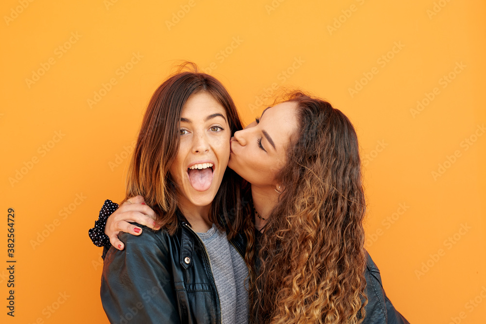 Cheerful girl sticking out tongue while her girlfriend kissing her in