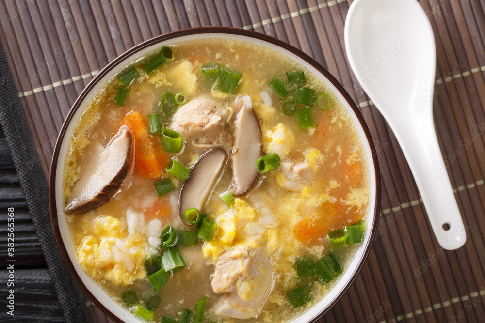 Zosui or ojiya is a mild and thin Japanese winter rice soup with egg, mushrooms, vegetables close-up in a bowl on the table. Horizontal top view from above