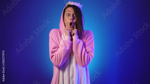 Positive girl in pink pajamas burst puffy cheeks with her palms
