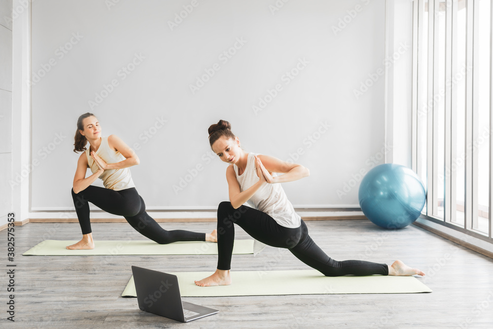 Two woman with laptop computer watching and learning yoga online from internet