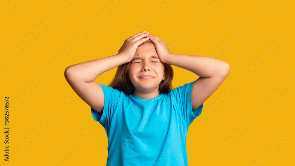 Anxious kid. Failure regret. Stress panic. Disappointment frustration. Portrait of troubled young girl in blue t-shirt suffering from headache with closed eyes isolated on orange background. Anxious kid. Failure regret. Stress panic. Disappointment frustration. Portrait of troubled young girl in blue t-shirt suffering from headache with closed eyes isolated on orange background.